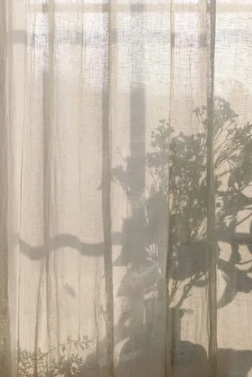 Zonlicht valt door een linnen gordijn, met de schaduw van een plant